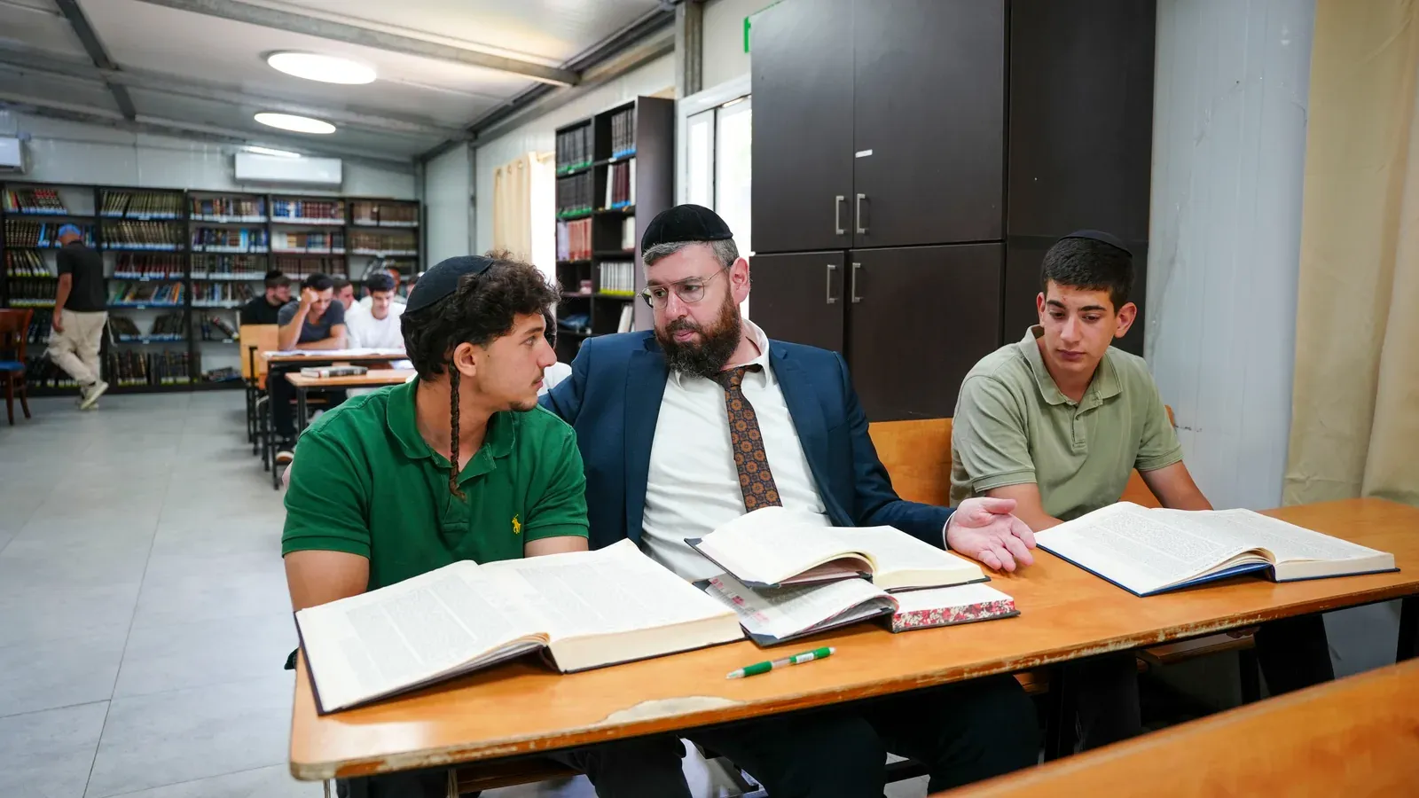 רב לומד גמרא עם שני תלמידים סביב שולחן בבית המדרש